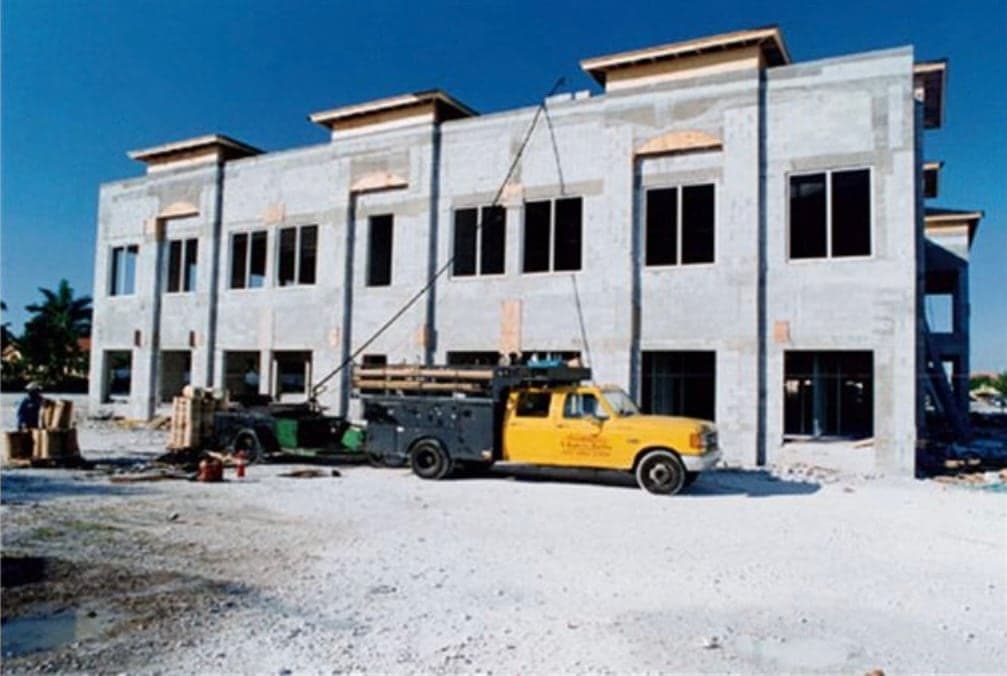 A yellow work truck at a two-story building still in bare block.