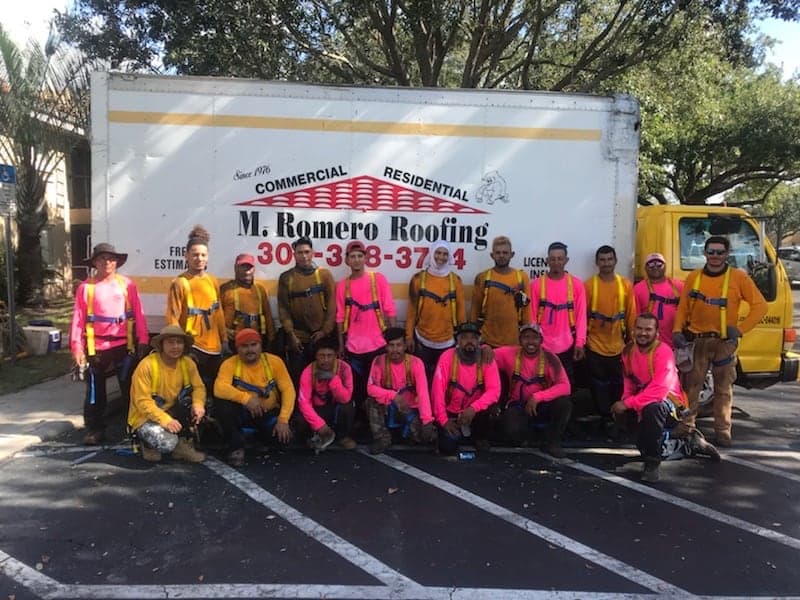 The M. Romero's Roofing crew in the pink and hi-vis shirts they wear every October for breast cancer awareness, in front of the box truck.