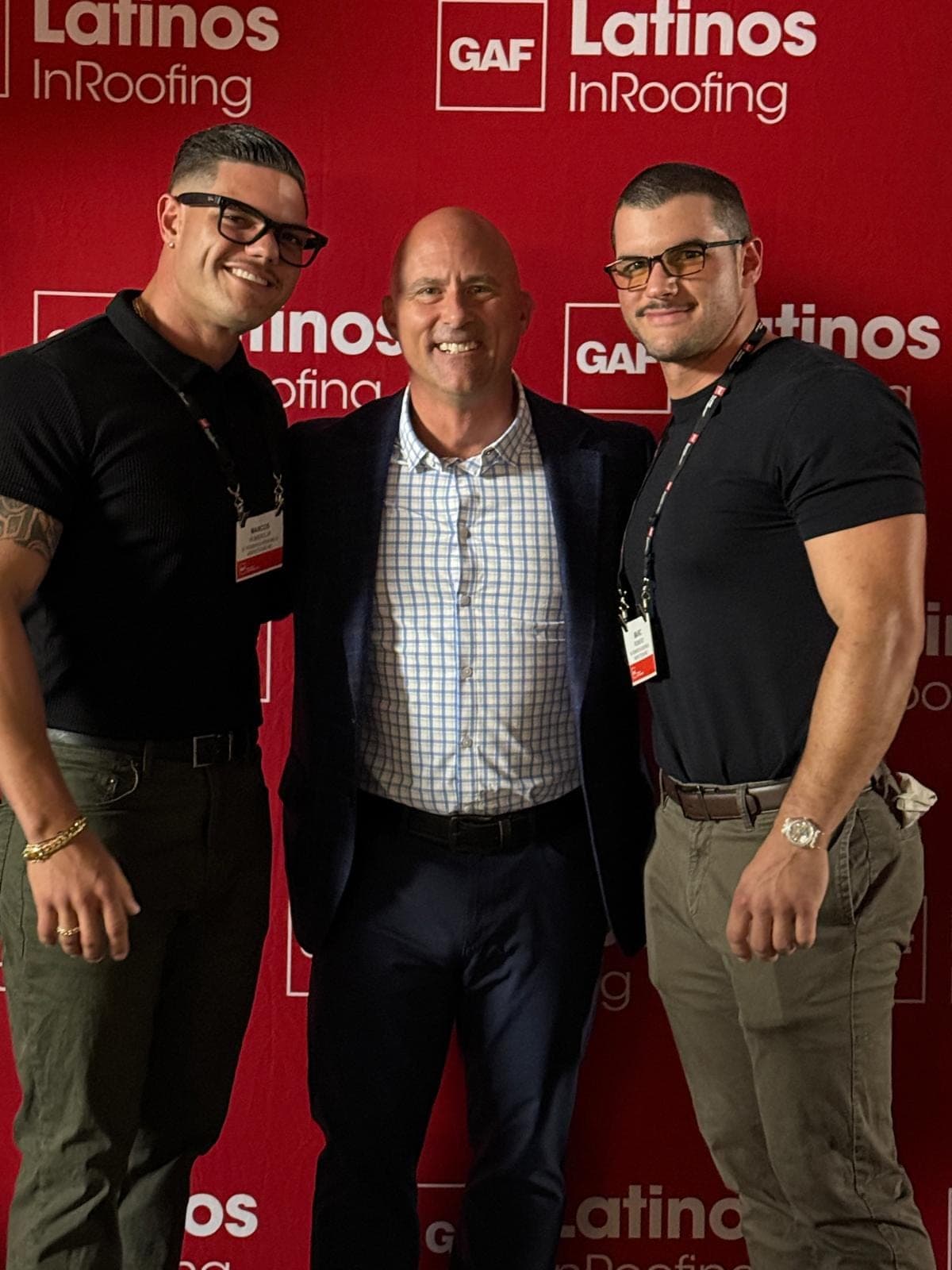 Three men stand together in front of a red GAF Latinos InRoofing backdrop.