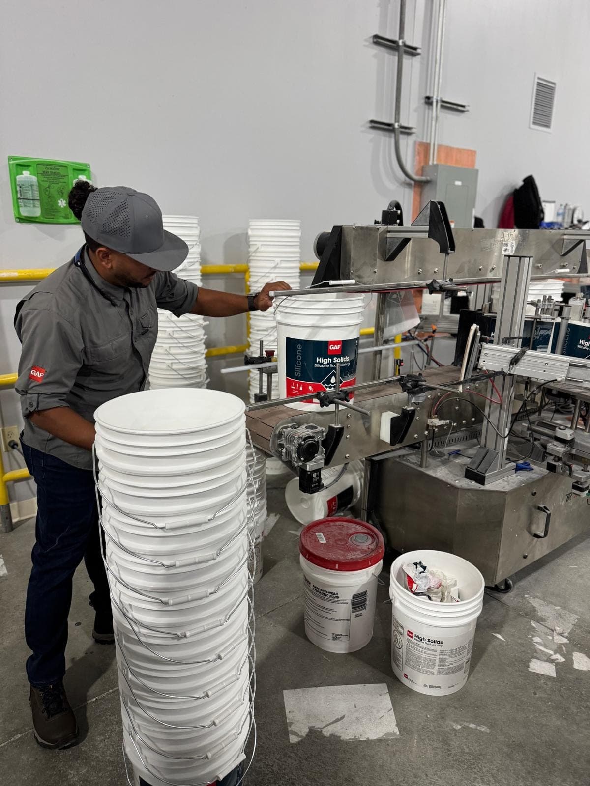 A worker guides white pails along a conveyor at a coatings plant.