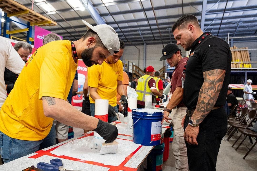 Workers apply coating at a long table during a hands on session.